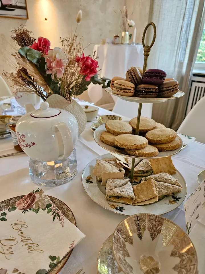 Festlich gedeckte Teetafel mit Kanne, Macarons, Gebäck und Sandwiches auf einer Etagere