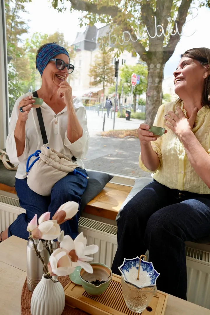 Maria und ein Gast genießen gemeinsam Tee am Fenster des Salons
