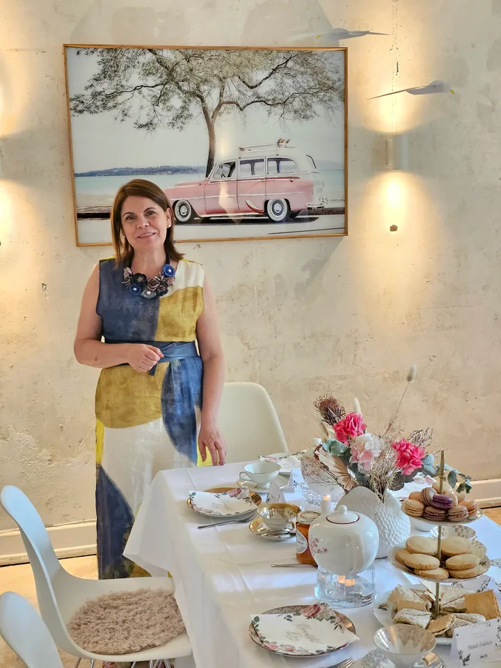 Maria Moreno steht neben einer liebevoll gedeckten Teetafel mit Porzellan, Gebäck und Blumen im Salon