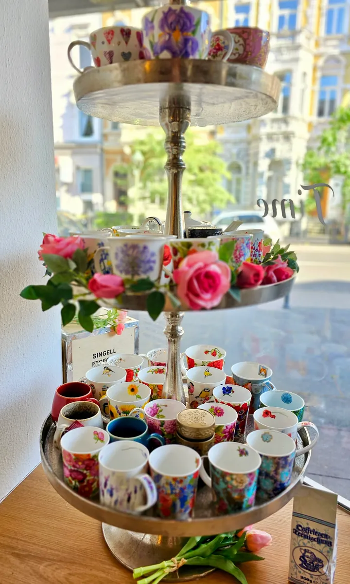 Florale Porzellantassen und rosa Rosen auf einer Etagere am Salonfenster